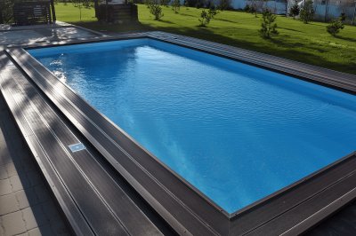 Прямоугольный бассейн с многоуровневым настилом и зелёным газоном на заднем плане